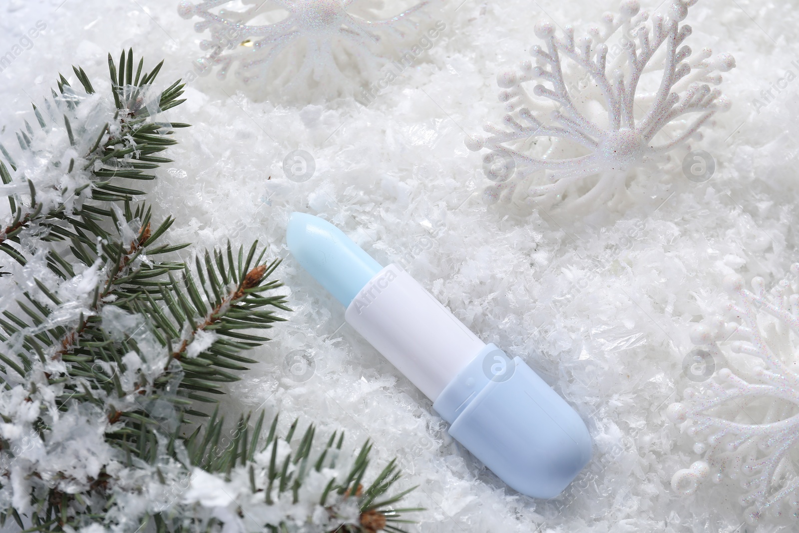 Photo of Moisturizing lip balm, Christmas decor and fir tree branches on artificial snow, flat lay. Winter care