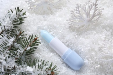 Photo of Moisturizing lip balm, Christmas decor and fir tree branches on artificial snow, flat lay. Winter care