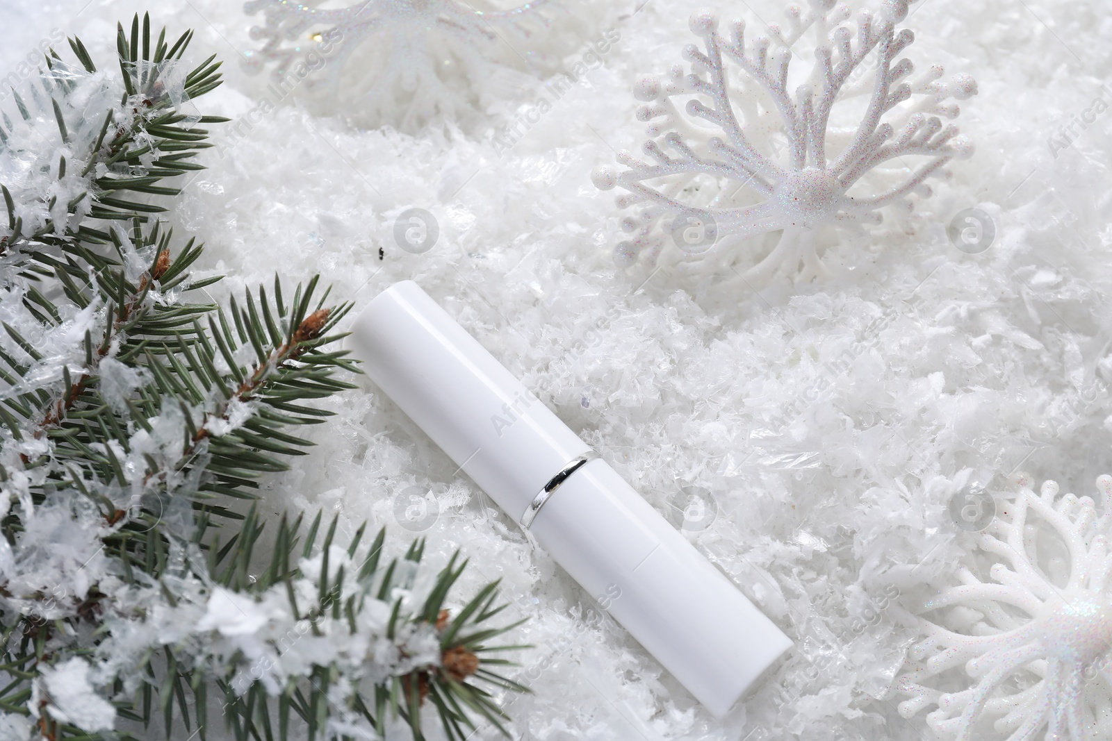 Photo of Moisturizing lip balm, Christmas decor and fir tree branches on artificial snow, flat lay. Winter care