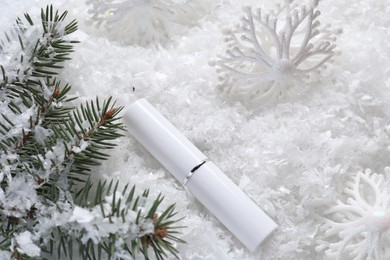 Photo of Moisturizing lip balm, Christmas decor and fir tree branches on artificial snow, flat lay. Winter care