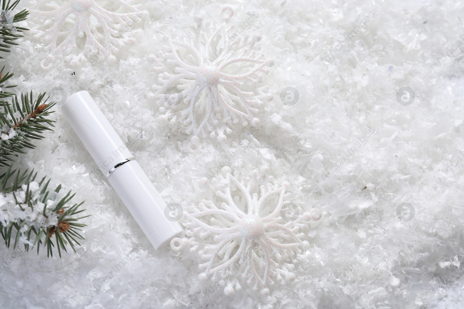 Photo of Moisturizing lip balm, Christmas decor and fir tree branches on artificial snow, flat lay. Space for text