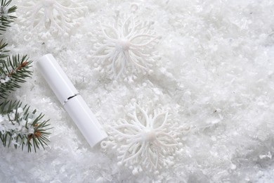 Photo of Moisturizing lip balm, Christmas decor and fir tree branches on artificial snow, flat lay. Space for text
