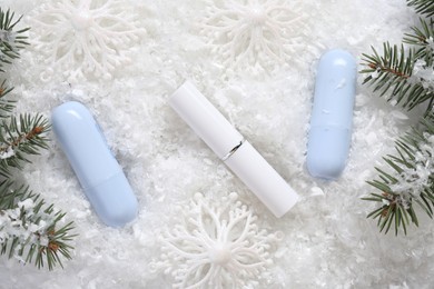 Photo of Moisturizing lip balms, Christmas decor and fir tree branches on artificial snow, flat lay. Winter care