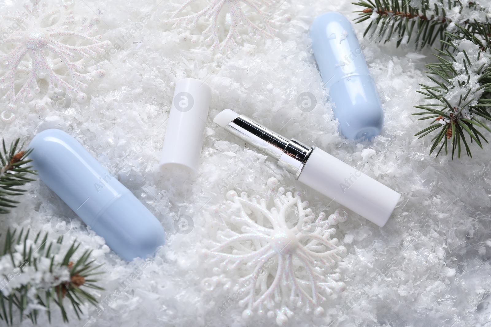 Photo of Moisturizing lip balms, Christmas decor and fir tree branches on artificial snow, above view. Winter care