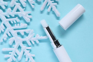 Photo of Moisturizing lip balm and Christmas decor on light blue background, flat lay. Winter care