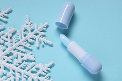 Photo of Moisturizing lip balm and Christmas decor on light blue background, flat lay. Winter care