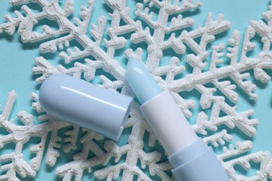 Photo of Moisturizing lip balm and Christmas decor on light blue background, flat lay. Winter care
