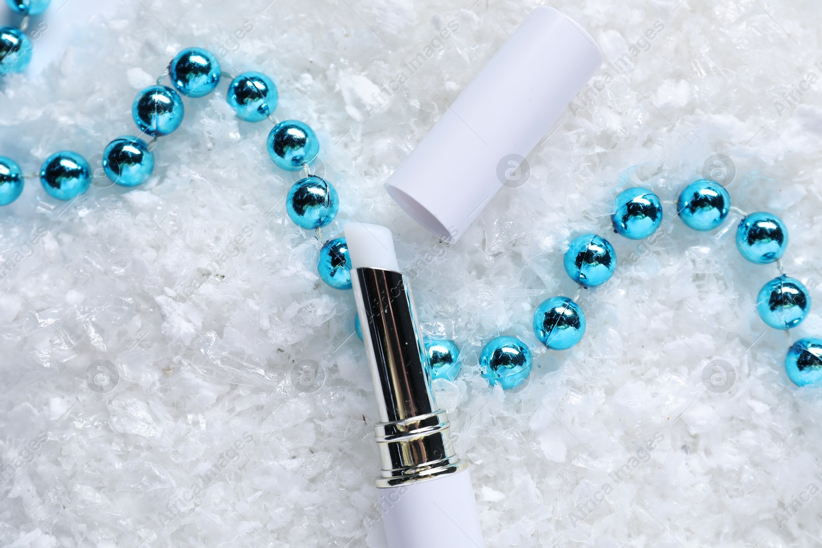 Photo of Moisturizing lip balm and Christmas decor on artificial snow, flat lay. Winter care