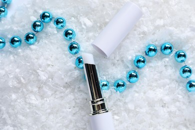 Photo of Moisturizing lip balm and Christmas decor on artificial snow, flat lay. Winter care