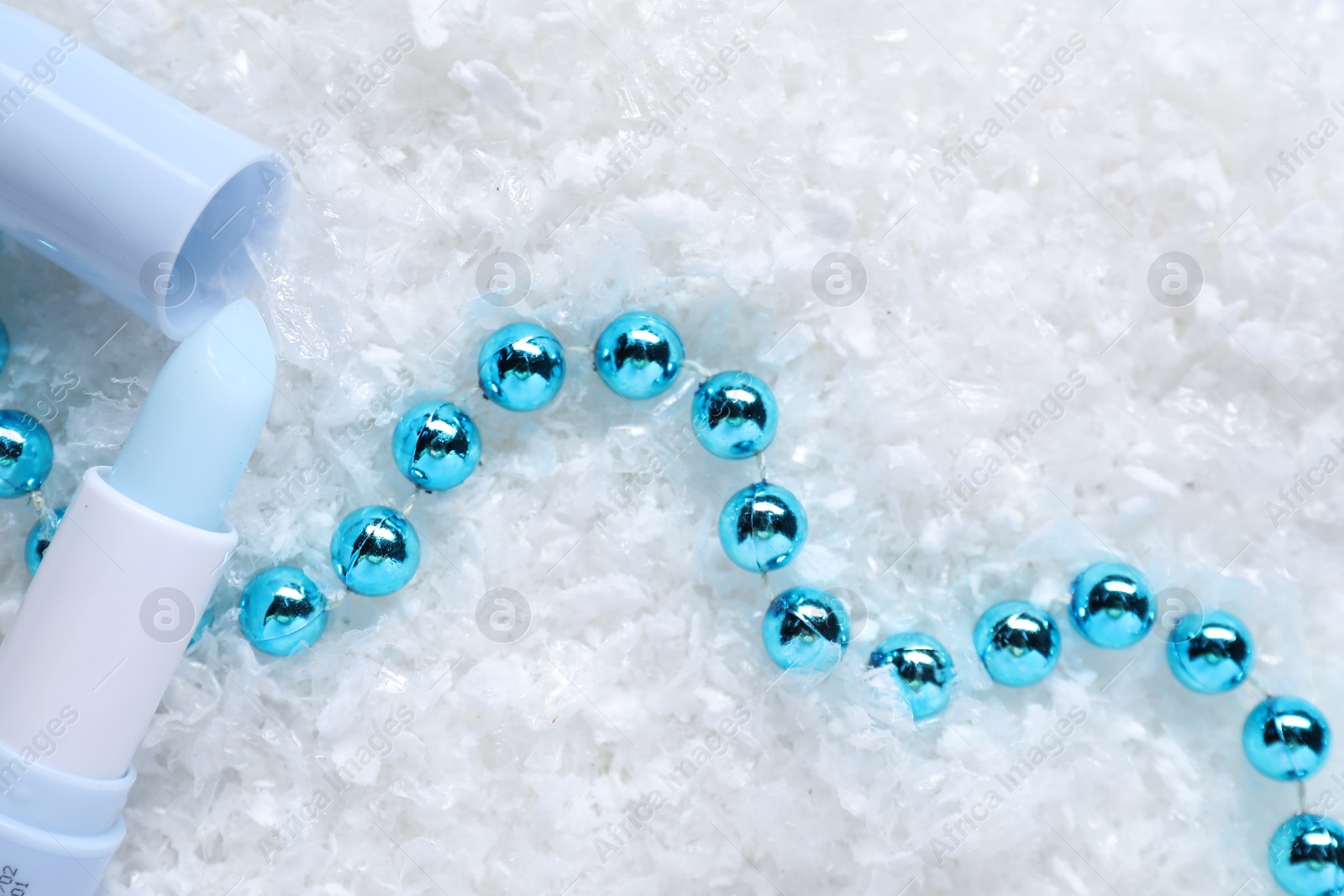 Photo of Moisturizing lip balm and Christmas decor on artificial snow, flat lay. Winter care