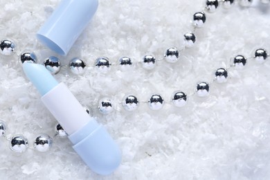 Photo of Moisturizing lip balm and Christmas decor on artificial snow, flat lay. Winter care
