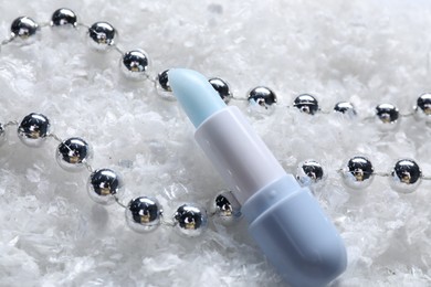 Photo of Moisturizing lip balm and Christmas decor on artificial snow, closeup. Winter care