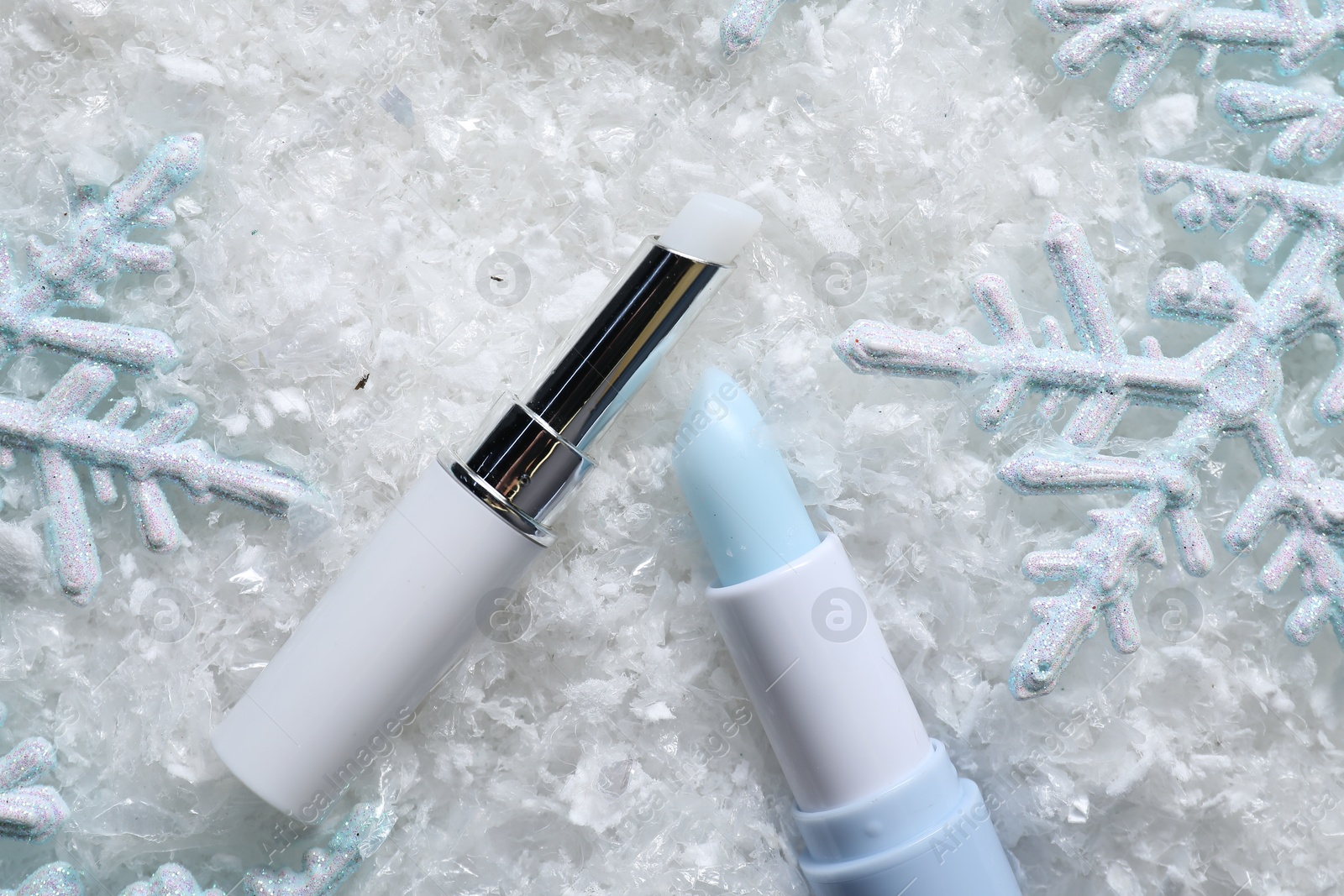 Photo of Moisturizing lip balm and Christmas decor on artificial snow, flat lay. Winter care