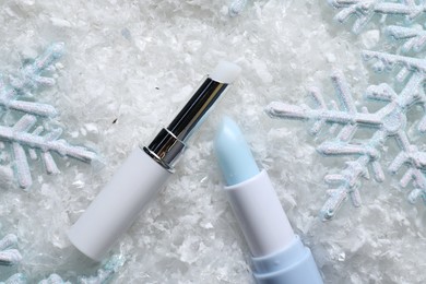Photo of Moisturizing lip balm and Christmas decor on artificial snow, flat lay. Winter care