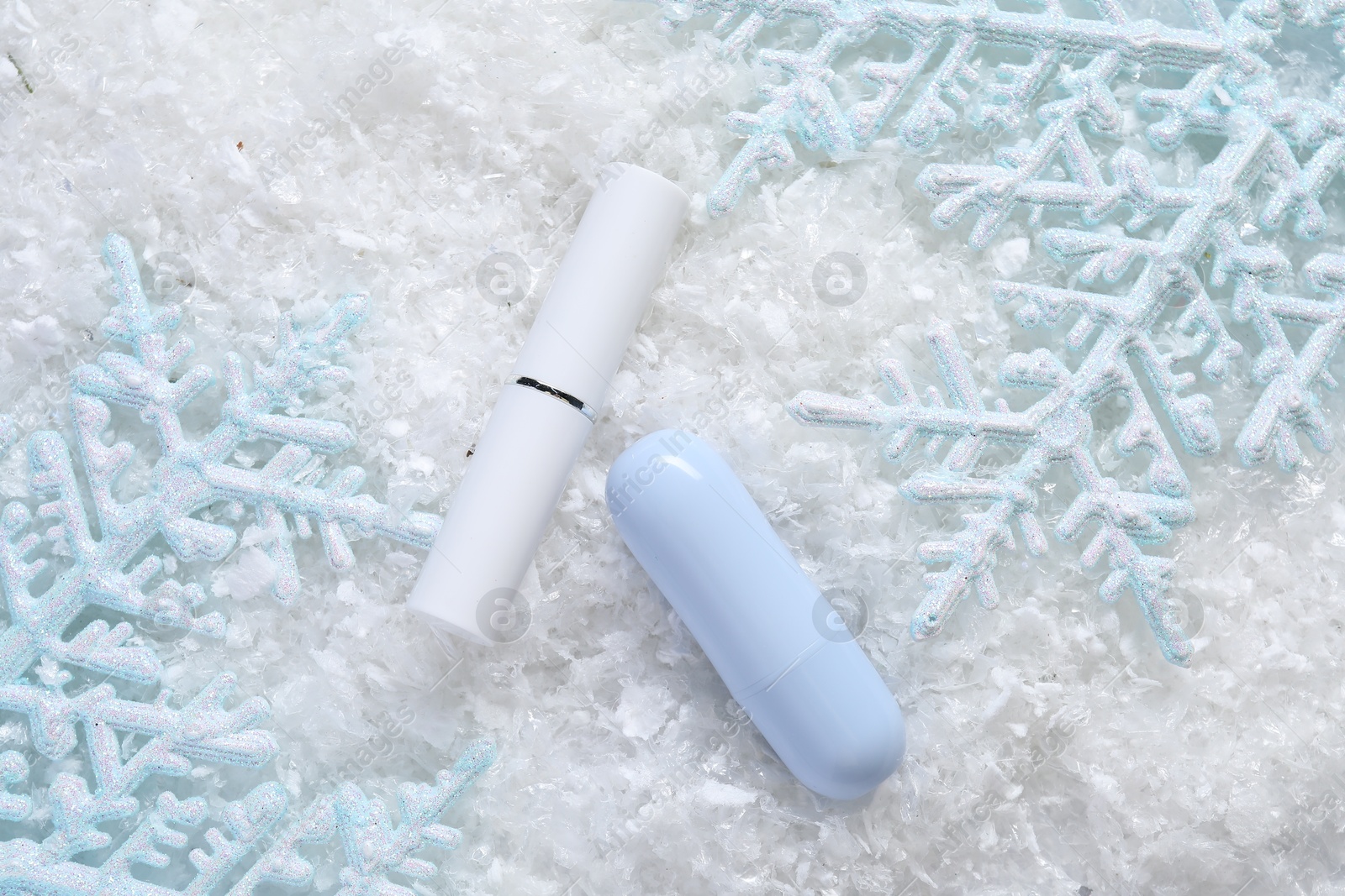 Photo of Moisturizing lip balm and Christmas decor on artificial snow, flat lay. Winter care