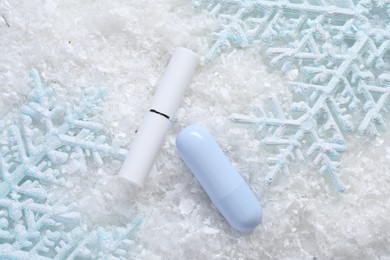 Photo of Moisturizing lip balm and Christmas decor on artificial snow, flat lay. Winter care