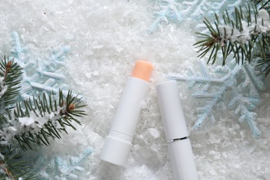 Photo of Moisturizing lip balms, Christmas decor and fir tree branches on artificial snow, flat lay. Winter care