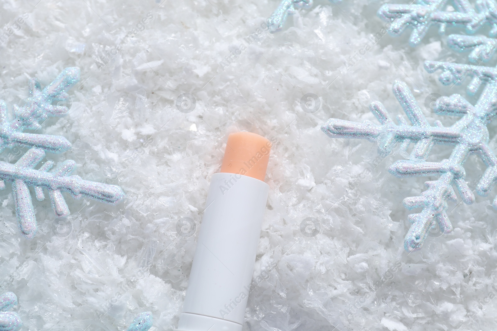 Photo of Moisturizing lip balm and Christmas decor on artificial snow, flat lay. Winter care