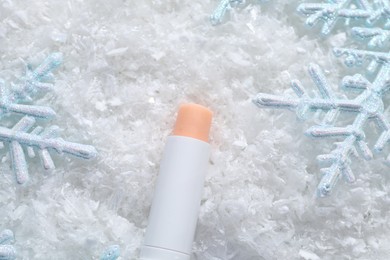 Photo of Moisturizing lip balm and Christmas decor on artificial snow, flat lay. Winter care
