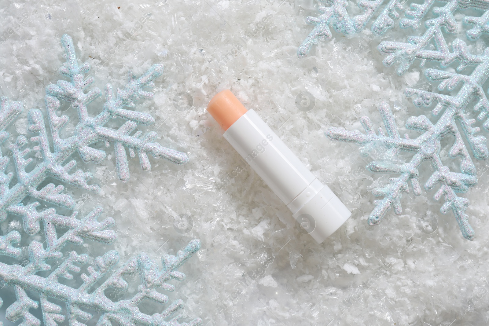 Photo of Moisturizing lip balm and Christmas decor on artificial snow, flat lay. Winter care