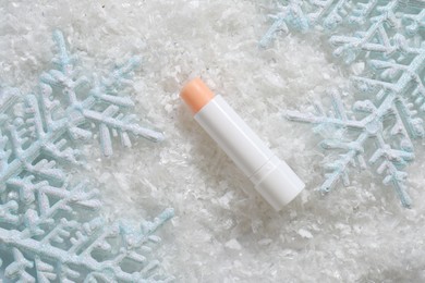 Photo of Moisturizing lip balm and Christmas decor on artificial snow, flat lay. Winter care