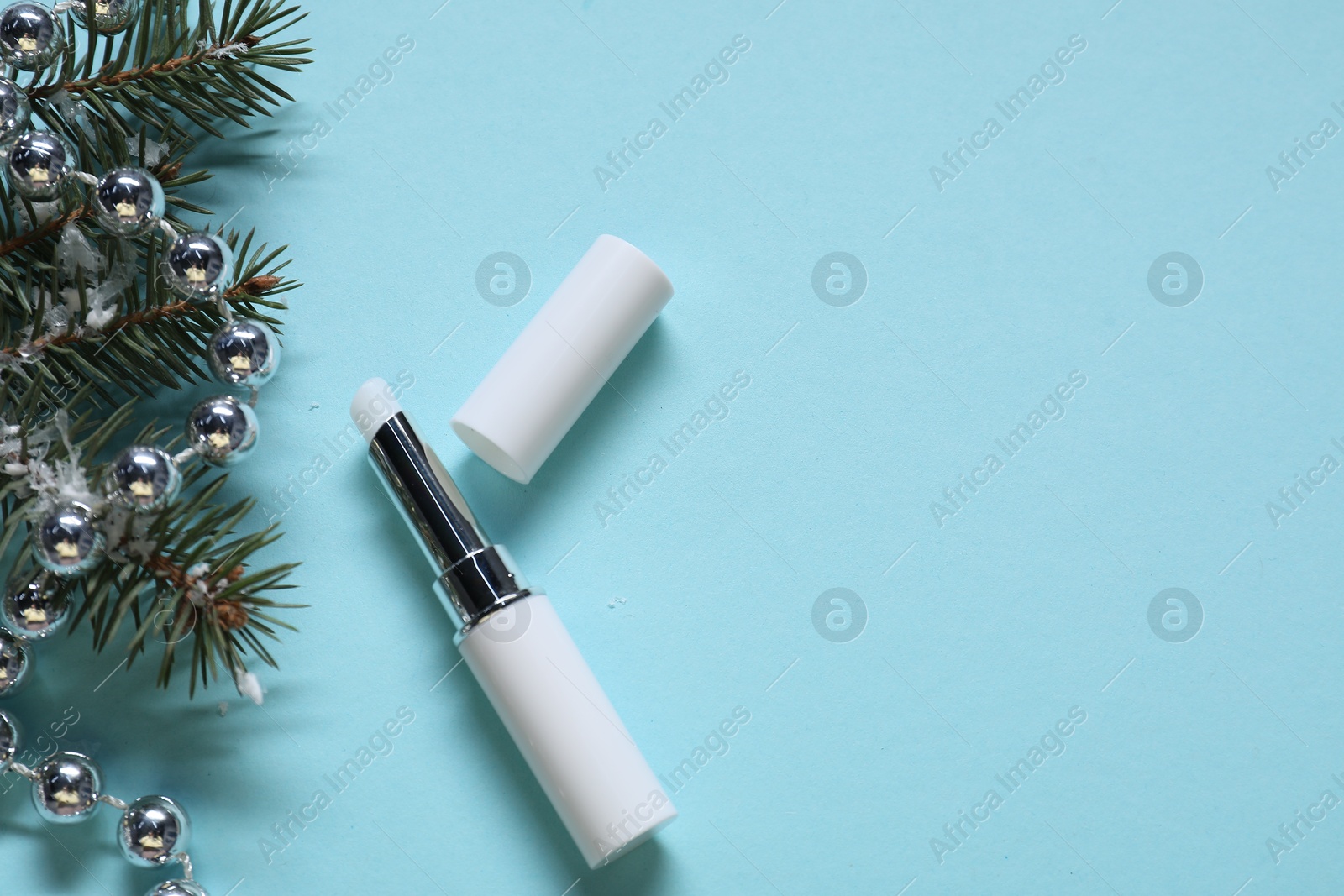 Photo of Moisturizing lip balm, Christmas decor and fir tree branches on light blue background, flat lay. Space for text