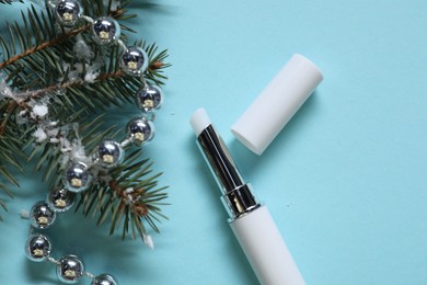 Photo of Moisturizing lip balm, Christmas decor and fir tree branches on light blue background, flat lay. Winter care