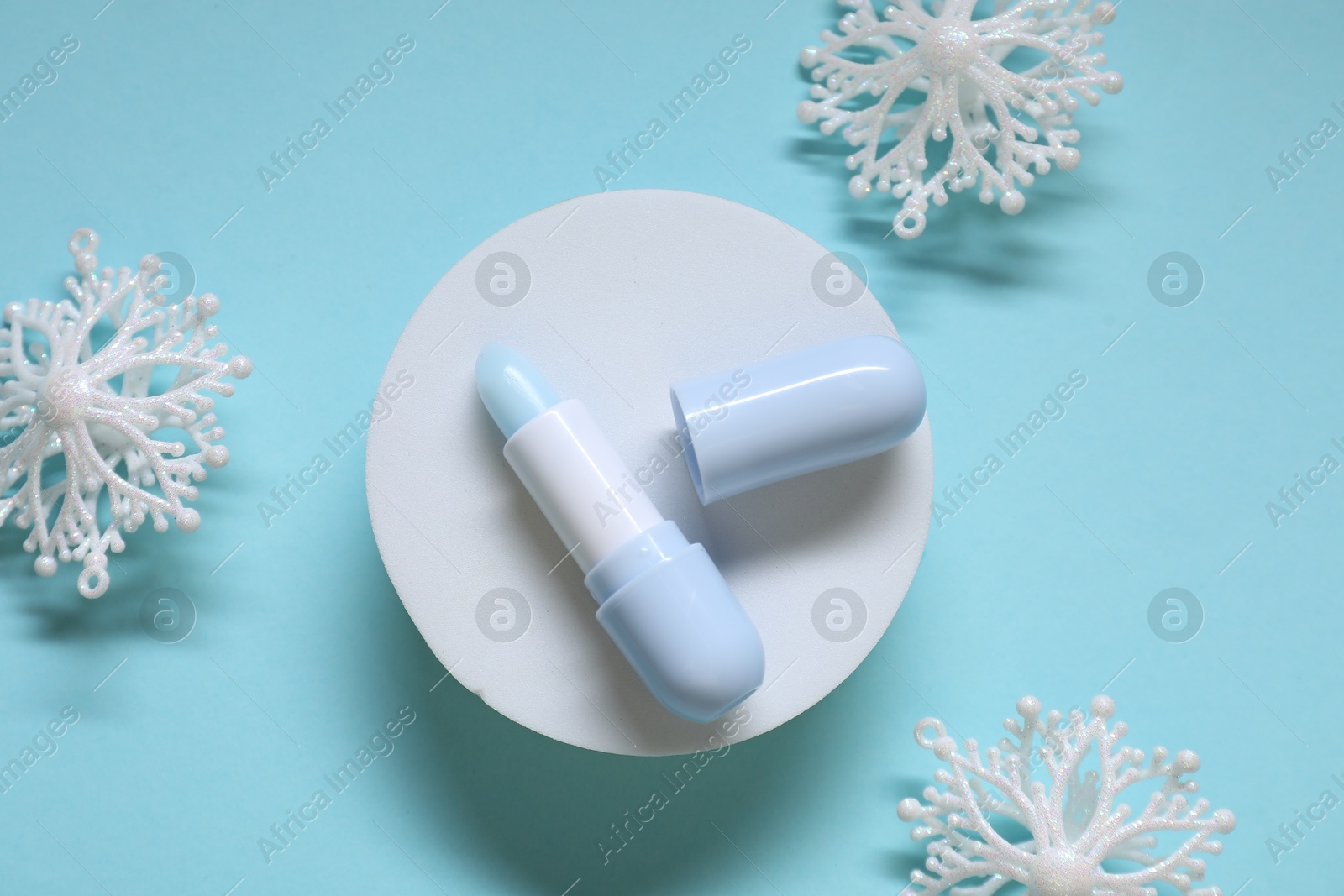 Photo of Moisturizing lip balm and Christmas decor on light blue background, flat lay. Winter care