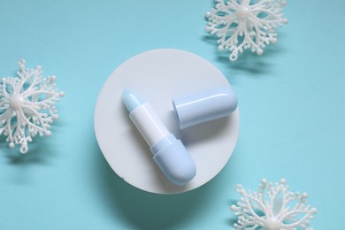 Photo of Moisturizing lip balm and Christmas decor on light blue background, flat lay. Winter care