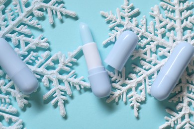 Photo of Moisturizing lip balm and Christmas decor on light blue background, flat lay. Winter care