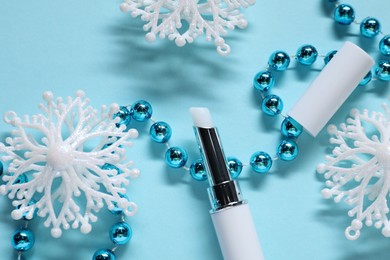 Photo of Moisturizing lip balm and Christmas decor on light blue background, flat lay. Winter care