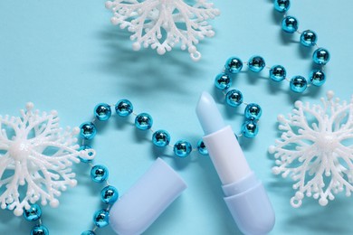 Photo of Moisturizing lip balm and Christmas decor on light blue background, flat lay. Winter care
