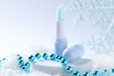 Photo of Moisturizing lip balm and Christmas decor on artificial snow, closeup. Winter care