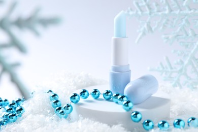 Photo of Moisturizing lip balm and Christmas decor on artificial snow, closeup. Winter care