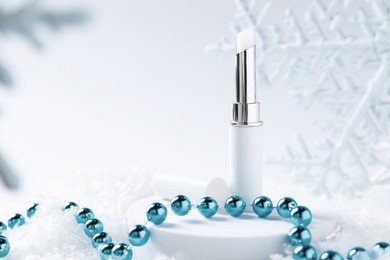 Photo of Moisturizing lip balm and Christmas decor on artificial snow, closeup. Space for text