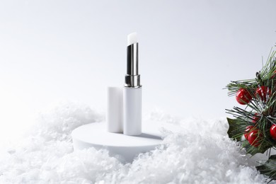 Photo of Moisturizing lip balm and Christmas decor on artificial snow. Winter care