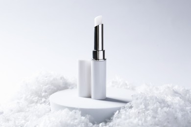 Photo of Moisturizing lip balm on artificial snow, closeup. Winter care