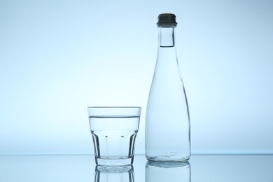Photo of Bottle and glass of water on mirror table against light blue gradient background