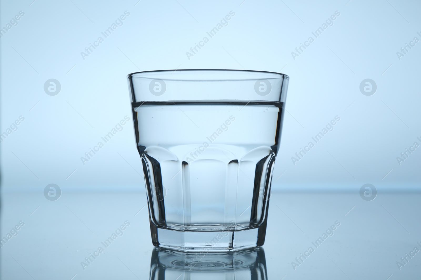 Fresh water in glass on mirror table against light blue gradient background, closeup Photo of Fresh water in glass on mirror table against light blue gradient background, closeup