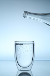 Photo of Bottle and glass of water on mirror table against light blue gradient background, closeup