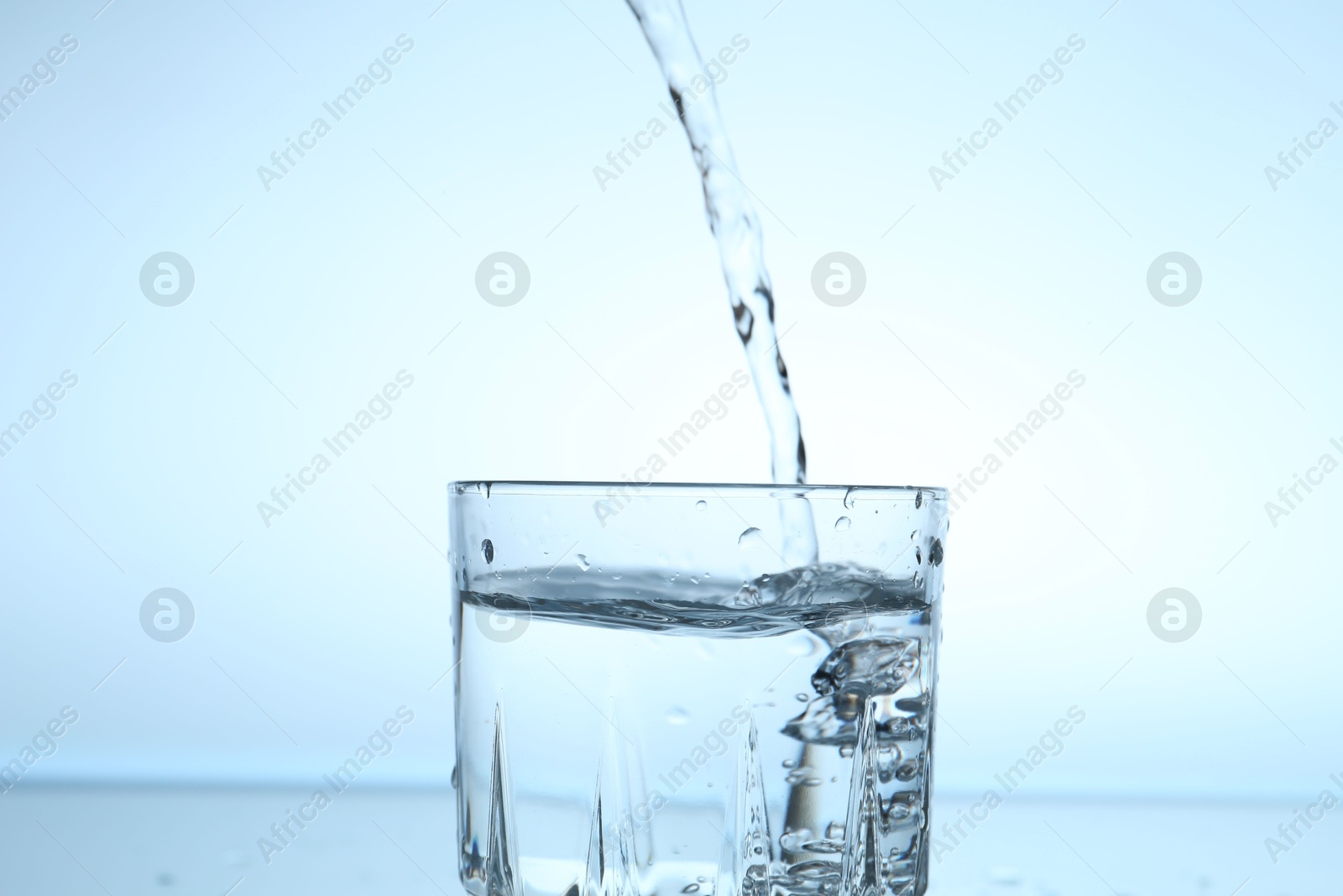 Pouring water into glass on light blue gradient background, closeup Photo of Pouring water into glass on light blue gradient background, closeup