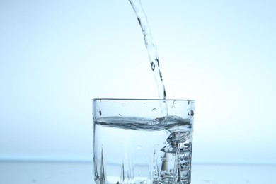 Photo of Pouring water into glass on light blue gradient background, closeup