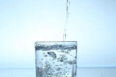 Photo of Pouring water into glass on light blue gradient background, closeup