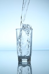 Photo of Pouring water into glass at mirror table against light blue gradient background, closeup