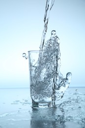 Photo of Pouring water into glass at mirror table against light blue gradient background, closeup