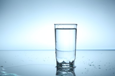 Photo of Fresh water in glass on mirror table against light blue gradient background