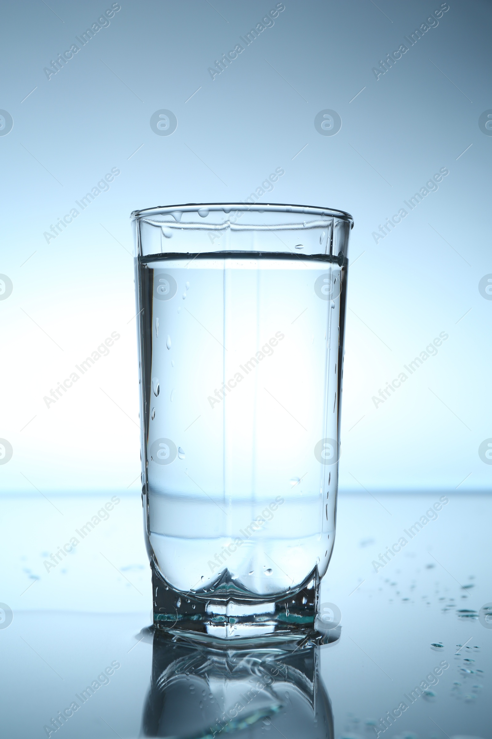 Fresh water in glass on mirror table against light blue gradient background, closeup Photo of Fresh water in glass on mirror table against light blue gradient background, closeup