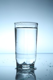 Photo of Fresh water in glass on mirror table against light blue gradient background, closeup