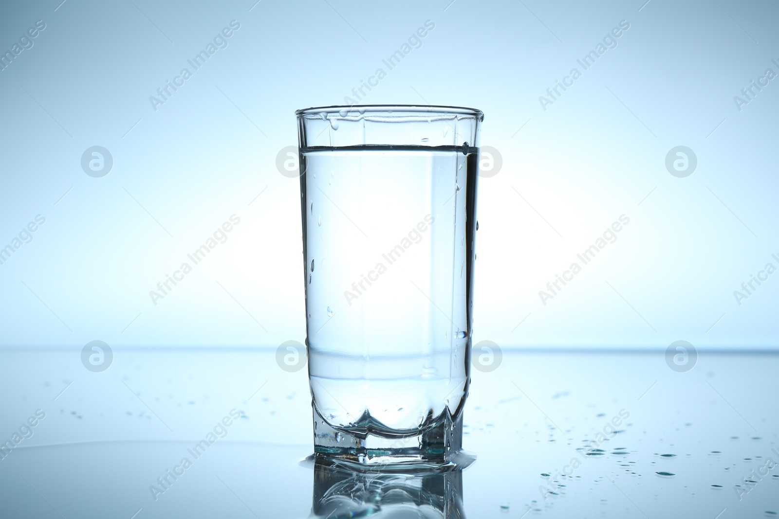 Fresh water in glass on mirror table against light blue gradient background, closeup Photo of Fresh water in glass on mirror table against light blue gradient background, closeup