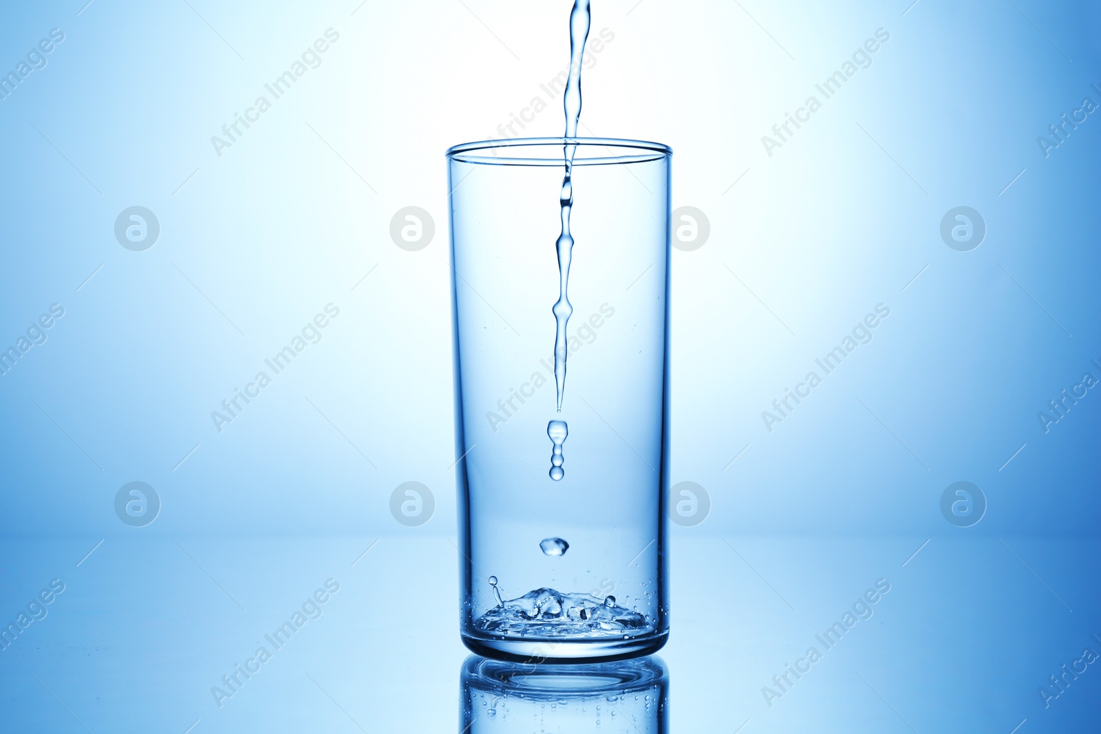 Photo of Pouring water into glass at mirror table against light blue gradient background, closeup